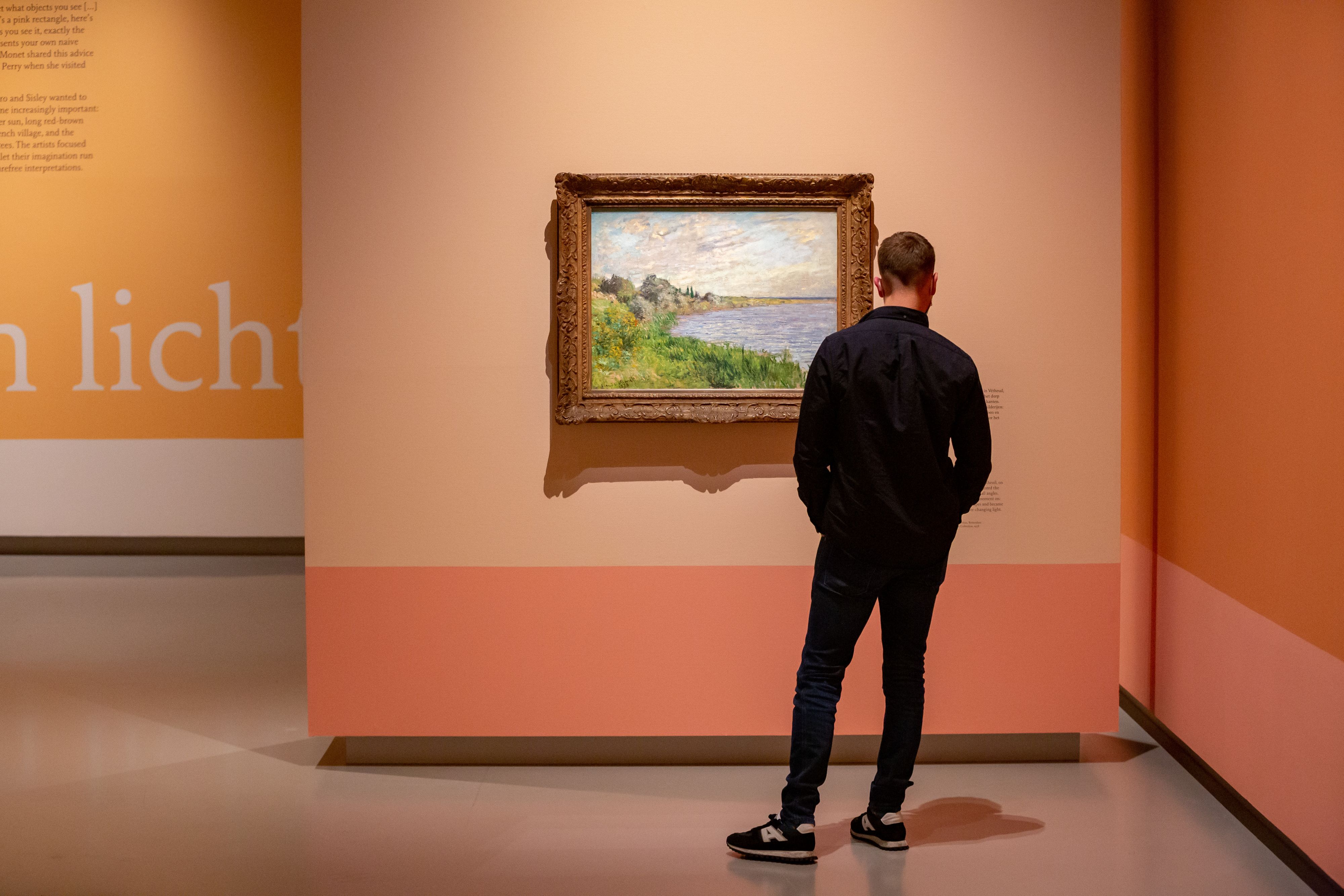 Een museumgast staat in een gele zaal van het Fries Museum een schilderij van een landschap te bekijken.