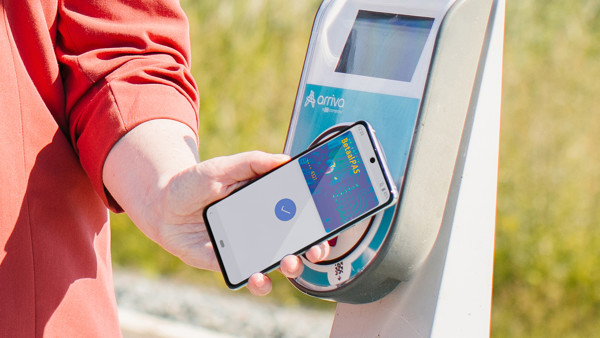Iemand houdt een smartphone met daarop een betaalpas voor een incheckpaal op het station. Iemand houdt een smartphone met daarop een betaalpas voor een incheckpaal op het station.