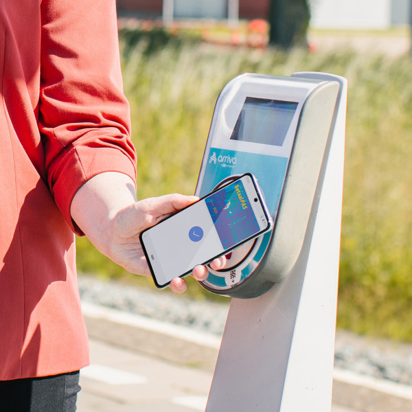 Iemand houdt een smartphone met daarop een betaalpas voor een incheckpaal op het station. Iemand houdt een smartphone met daarop een betaalpas voor een incheckpaal op het station.