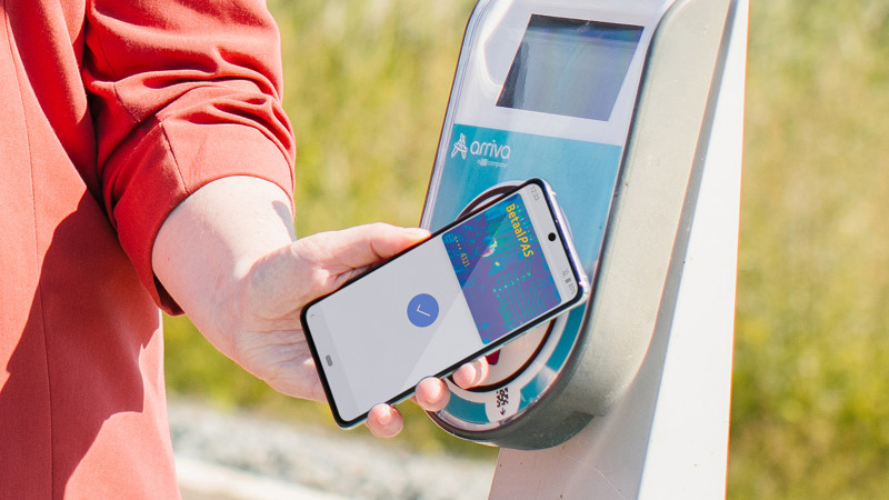 Iemand houdt een smartphone met daarop een betaalpas voor een incheckpaal op het station. Iemand houdt een smartphone met daarop een betaalpas voor een incheckpaal op het station.