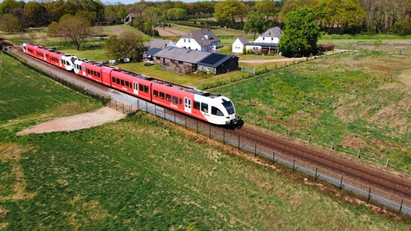 Een rode trein van Arriva vanaf boven bekeken, rijdt door een groen landschap met wat boerderijen. Een rode trein van Arriva vanaf boven bekeken, rijdt door een groen landschap met wat boerderijen.