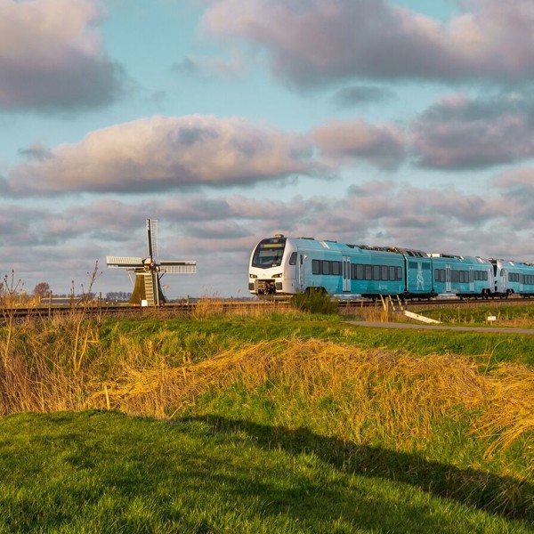Een groenwitte dieseltrein van Arriva rijdt door een vlak Nederlands landschap met een ouderwetse molen op de achtergrond. Een groenwitte dieseltrein van Arriva rijdt door een vlak Nederlands landschap met een ouderwetse molen op de achtergrond.
