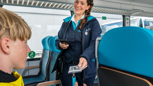 Conductrice met vlecht in haar en in Arriva-uniform controleert de OV-chipkaart van een jonge reiziger. Conductrice met vlecht in haar en in Arriva-uniform controleert de OV-chipkaart van een jonge reiziger.