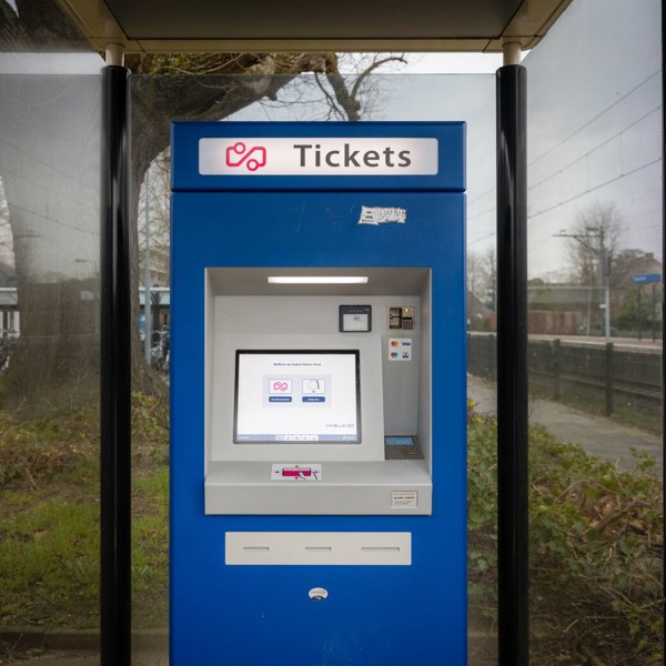 Blauwe ticketautomaat met touchscreen onder een overkapping op een treinperron. Blauwe ticketautomaat met touchscreen onder een overkapping op een treinperron.