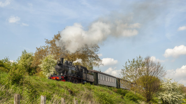 Een ouderwetse zwarte stoomtrein rijdt door een groen Limburgs landschap. Een ouderwetse zwarte stoomtrein rijdt door een groen Limburgs landschap.