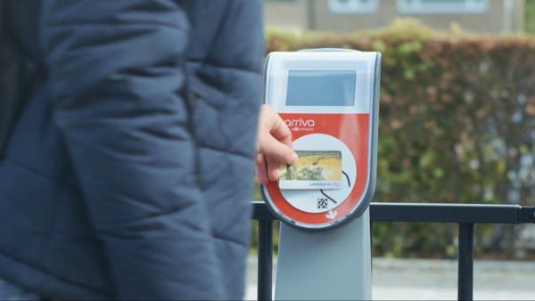 Iemand in een warme jas houdt een ov-chipkaart bij de incheckpaal. Iemand in een warme jas houdt een ov-chipkaart bij de incheckpaal.