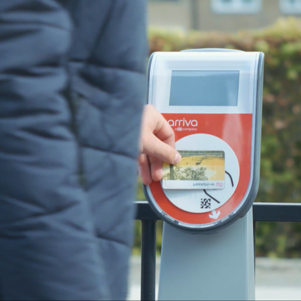 Iemand in een warme jas houdt een ov-chipkaart bij de incheckpaal. Iemand in een warme jas houdt een ov-chipkaart bij de incheckpaal.