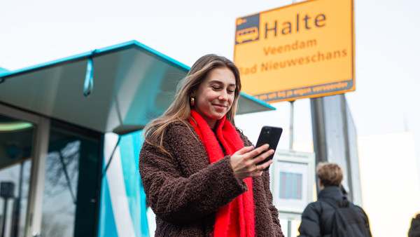 Vrouw kijkt op telefoon bij treinvervangende bushalte Vrouw kijkt op telefoon bij treinvervangende bushalte