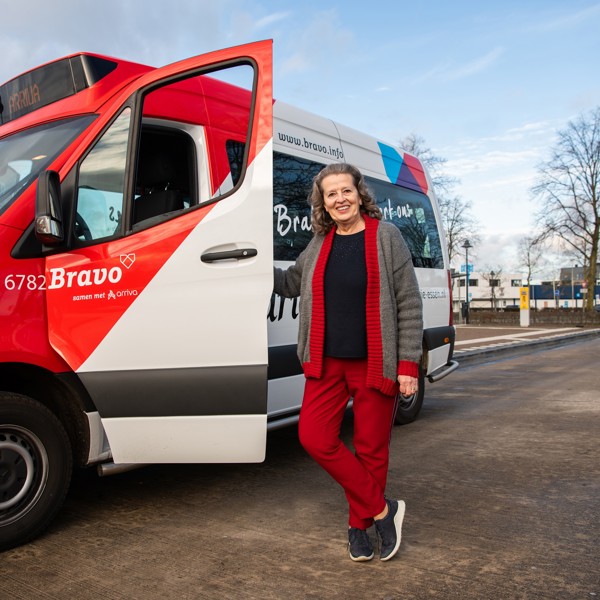 Lachende vrouw staat naast open deur van rood-wit buurtbusje in Brabant. Lachende vrouw staat naast open deur van rood-wit buurtbusje in Brabant.