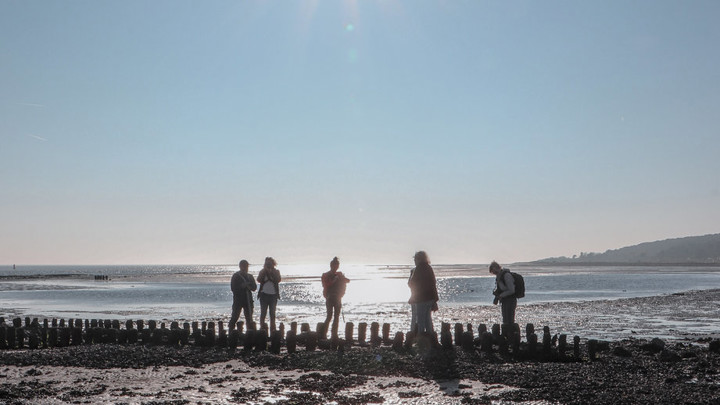 Vijf mensen staan op het drooggevallen wat op onder een felblauwe licht met zon hoog in de hemel. Vijf mensen staan op het drooggevallen wat op onder een felblauwe licht met zon hoog in de hemel.