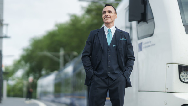 Machinist van Arriva glimlacht en kijkt in de verte met achter hem een trein. Machinist van Arriva glimlacht en kijkt in de verte met achter hem een trein.