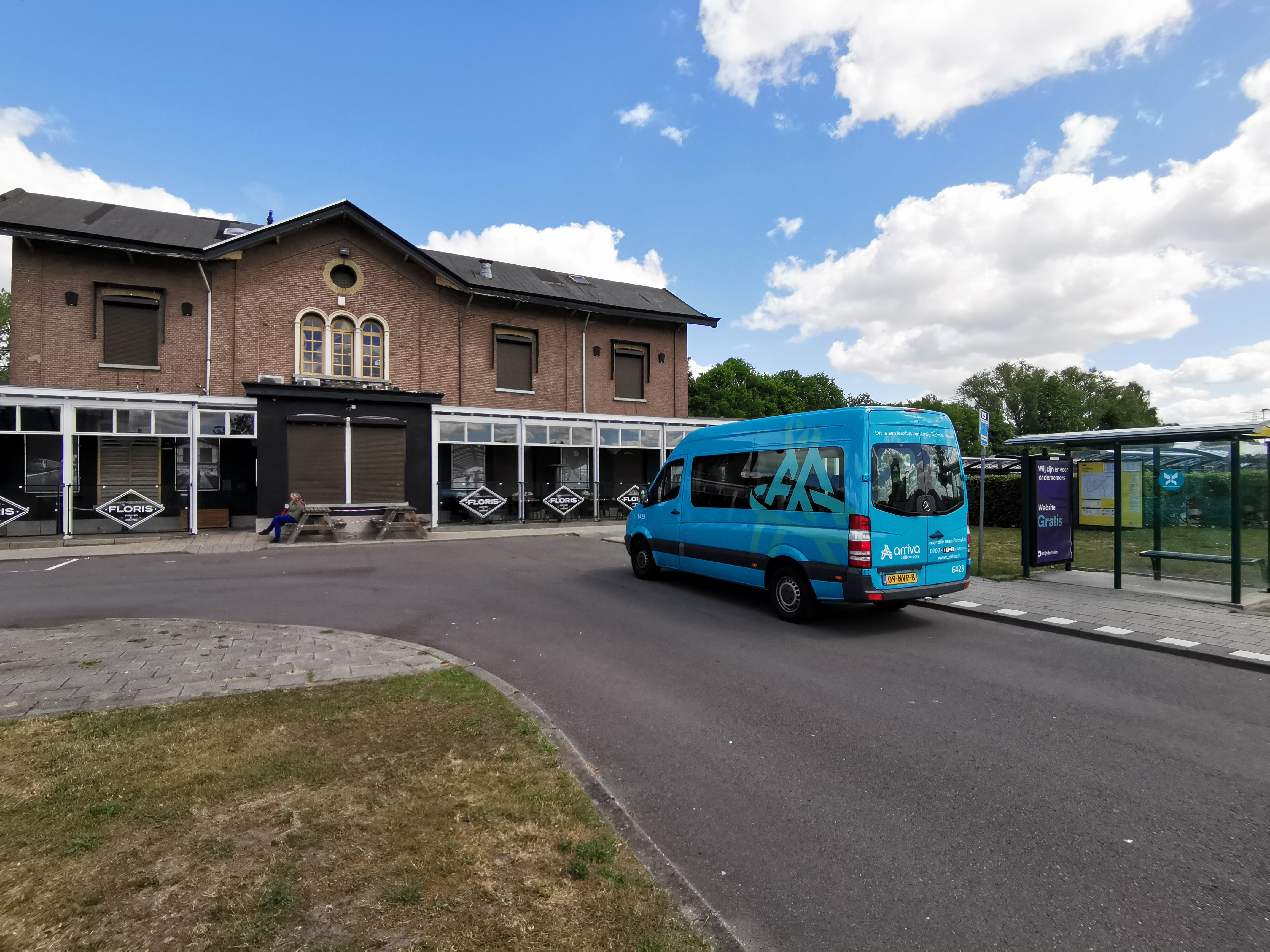 Kleine blauwe buurtbus staat geparkeerd bij een ouderwets, klein station.