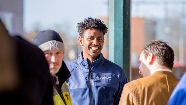 Een servicemedewerker staat lachend bij de bushalte. Een servicemedewerker staat lachend bij de bushalte.