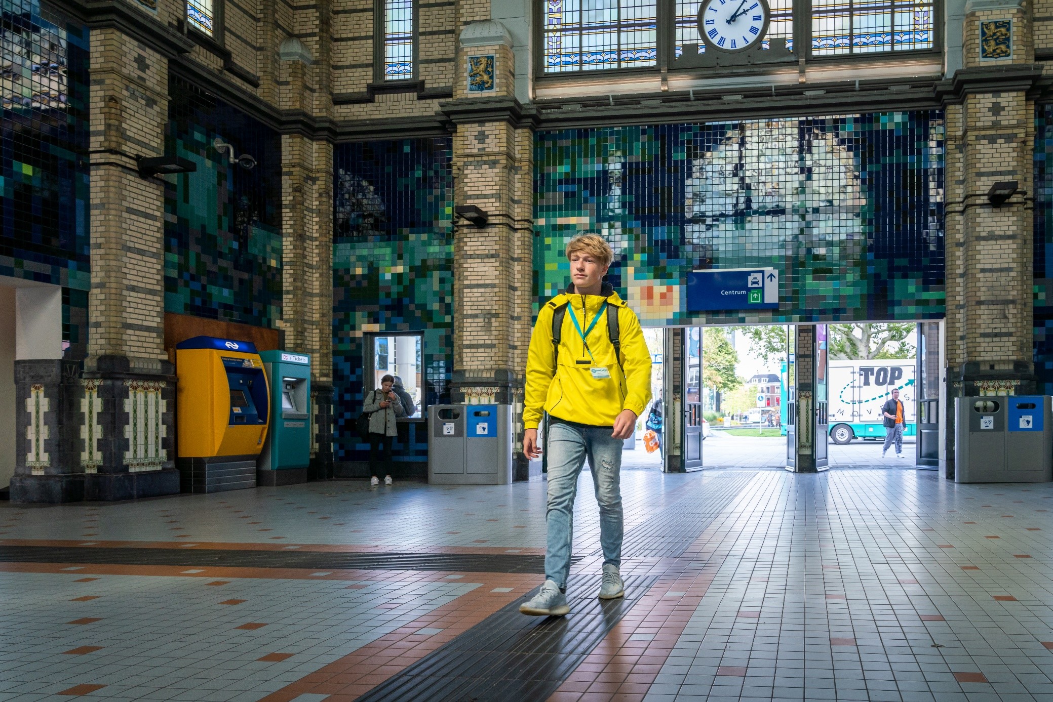 Jongen in gele jas loopt door een stationshal.