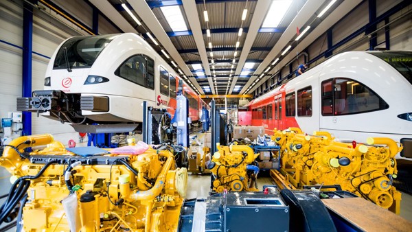 Twee Arriva treinen in een werkplaats met gele machines op de voorgrond. Twee Arriva treinen in een werkplaats met gele machines op de voorgrond.