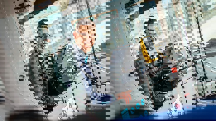 Een mannelijke buschauffeur met een bril zit achter het stuur van een Arriva-bus en kijkt achterom. Een mannelijke buschauffeur met een bril zit achter het stuur van een Arriva-bus en kijkt achterom.