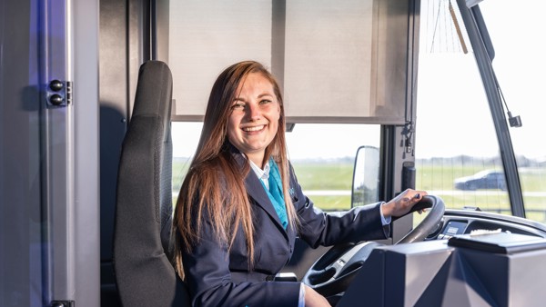 Vrouwelijke buschauffeur met lang haar en in uniform zit lachend achter het stuur van haar Arriva-bus. Vrouwelijke buschauffeur met lang haar en in uniform zit lachend achter het stuur van haar Arriva-bus.