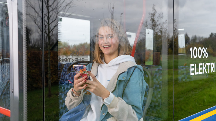 Jonge meid zit in een bus in Limburg met haar telefoon en kijkt lachend naar buiten Jonge meid zit in een bus in Limburg met haar telefoon en kijkt lachend naar buiten