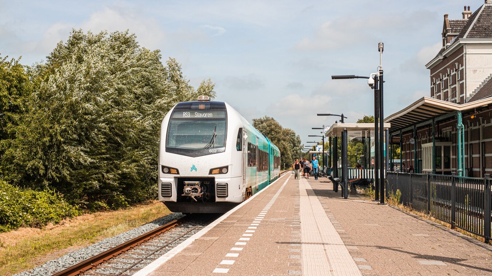Blauwe Arriva trein staat stil in de zon langs het perron van een klein station.