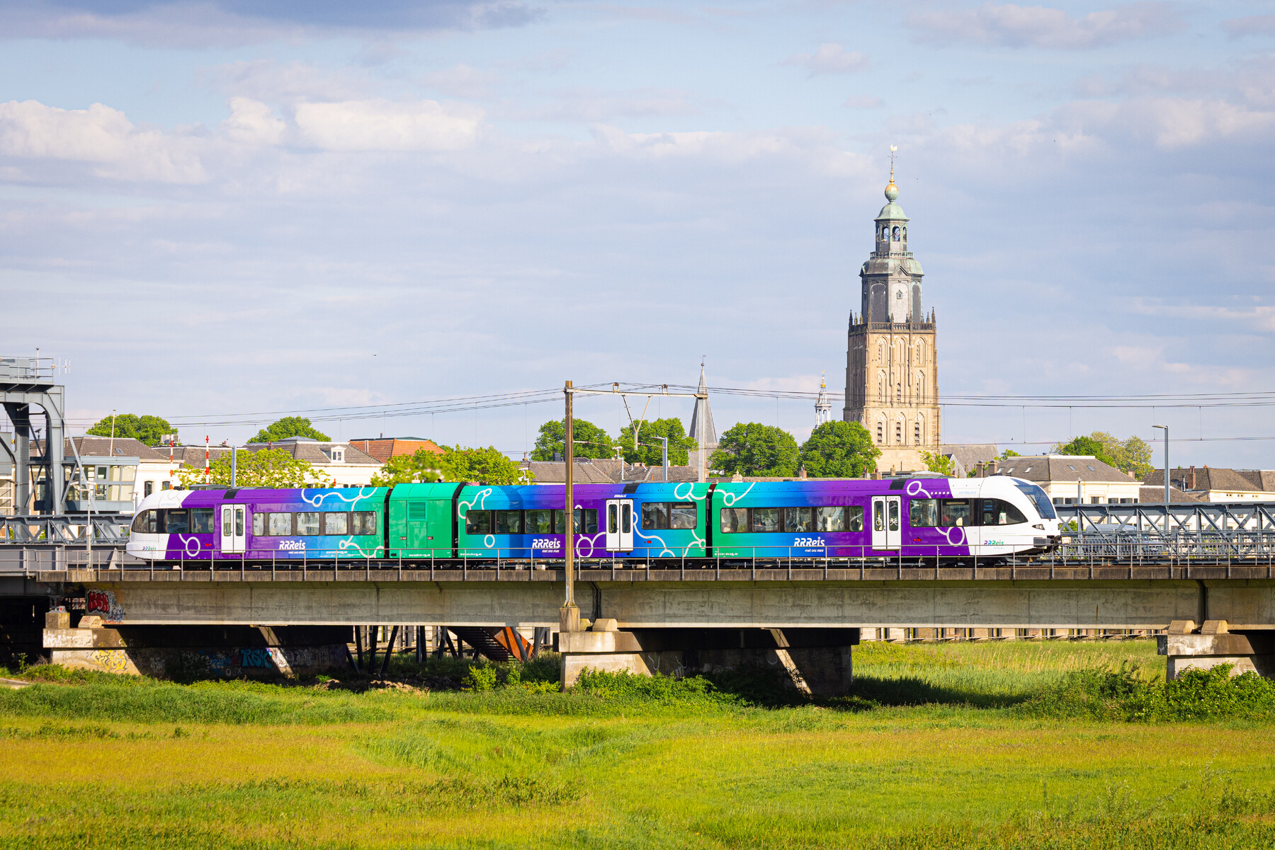een trein in de RRReiskleuren paars blauw groen op de rails in het Achterhoekse landschap 