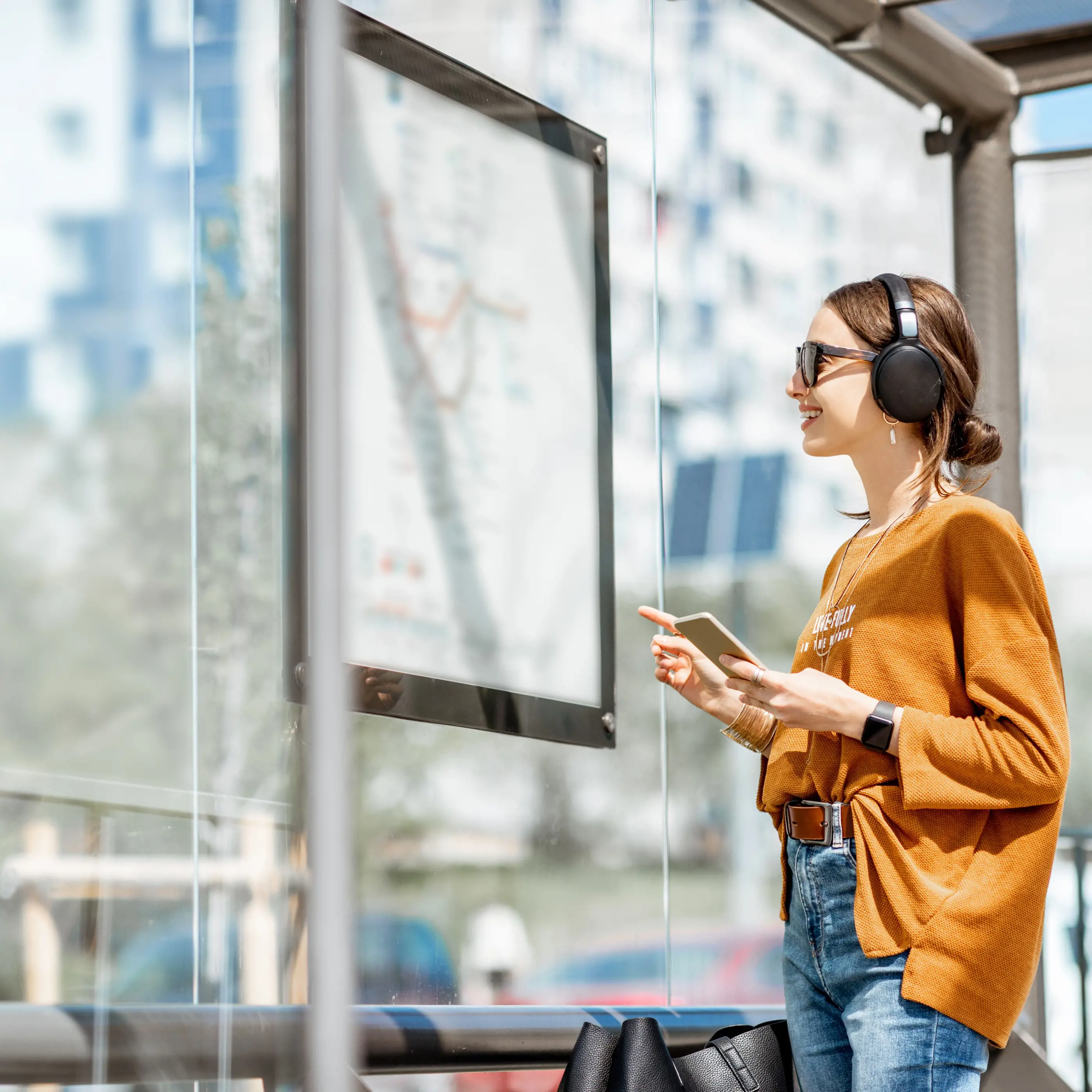 Lachende reiziger staat met koptelefoon op naar de bustijden te kijken op de bushalte.