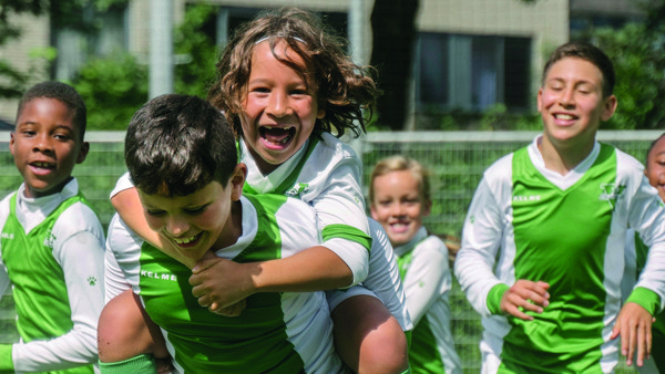 Jongens en meisjes van een jaar of 7 rennen in sporttenue. Vooraan springt een kind op de rug van een ander kind. Jongens en meisjes van een jaar of 7 rennen in sporttenue. Vooraan springt een kind op de rug van een ander kind.