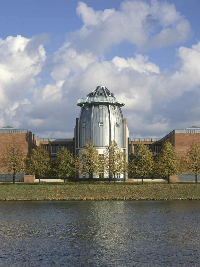 Een vergezicht van het Bonnefanten Museum in Maastricht, een metalen, eivormig gebouw aan de rivier.