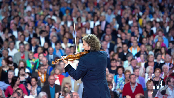 Andre Rieu vanaf de rug gezien speelt in pak viool voor honderden toeschouwers op een tribune. Andre Rieu vanaf de rug gezien speelt in pak viool voor honderden toeschouwers op een tribune.