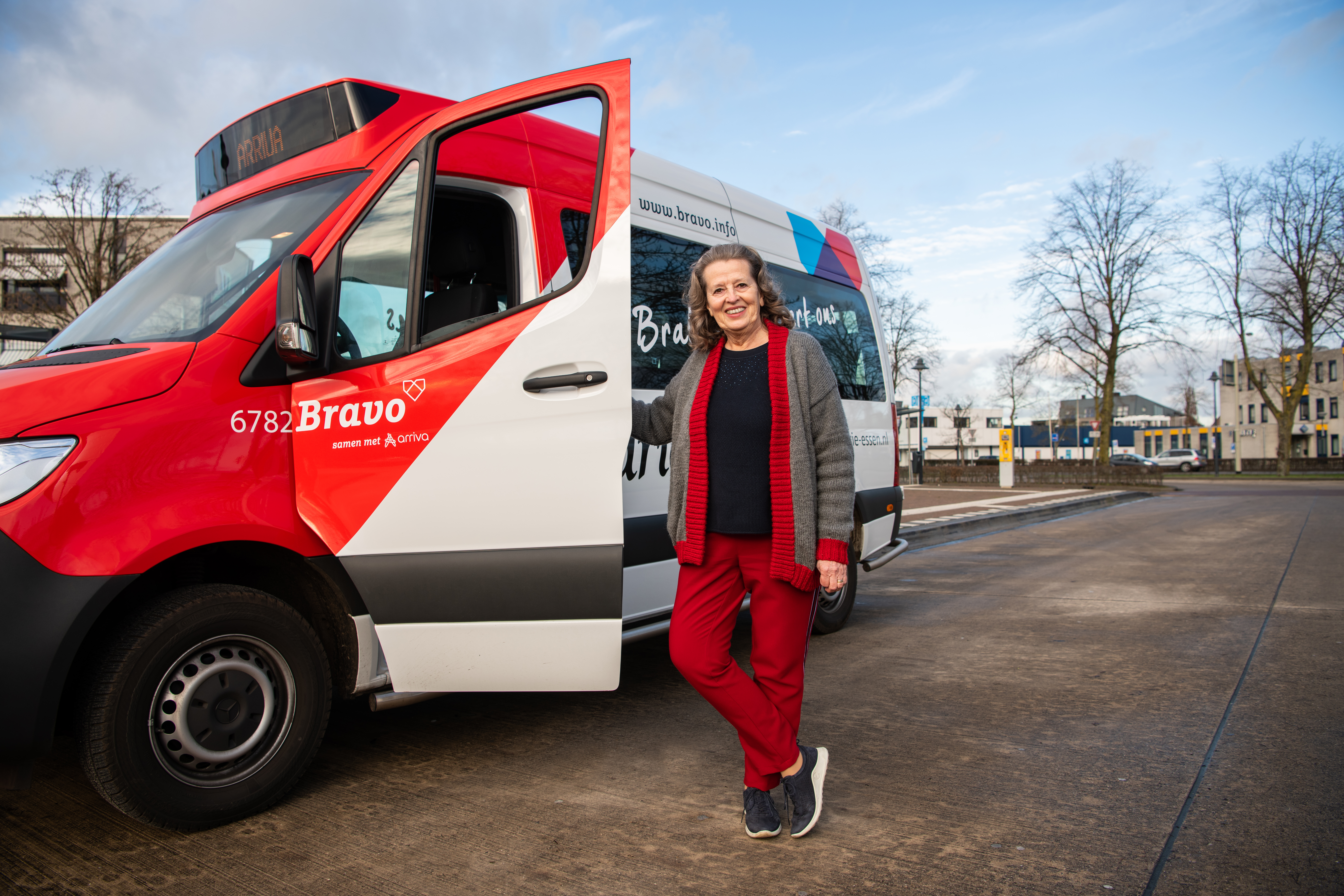 Vrouw staat lachend naast rood-witte buurtbus in Brabant