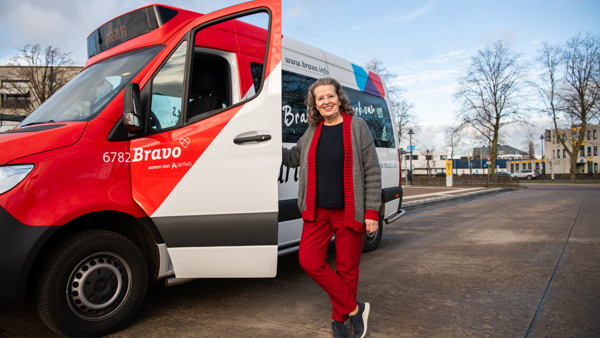 Vrouw staat lachend naast rood-witte buurtbus in Brabant Vrouw staat lachend naast rood-witte buurtbus in Brabant