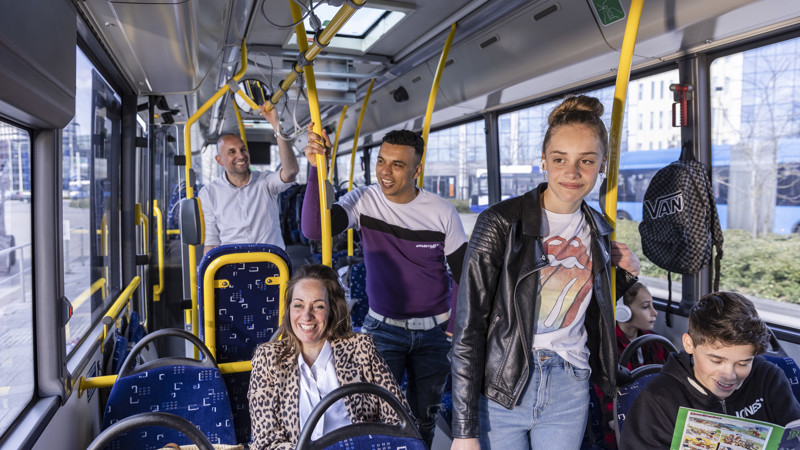 Meerdere reizigers die jong en hip gekleed zijn staan en zitten in een Arriva-bus en moeten lachen. Meerdere reizigers die jong en hip gekleed zijn staan en zitten in een Arriva-bus en moeten lachen.