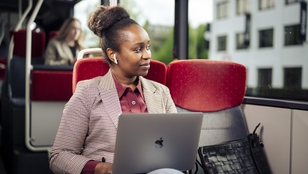 Een vrouw zit in de bus in pak met oordopjes in en laptop op schoot terwijl ze uit het raam kijkt. Een vrouw zit in de bus in pak met oordopjes in en laptop op schoot terwijl ze uit het raam kijkt.