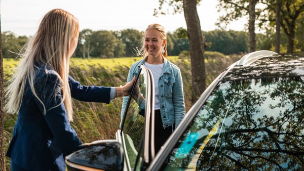 Twee jonge vrouwen staan lachen bij het open portier van een auto. Twee jonge vrouwen staan lachen bij het open portier van een auto.