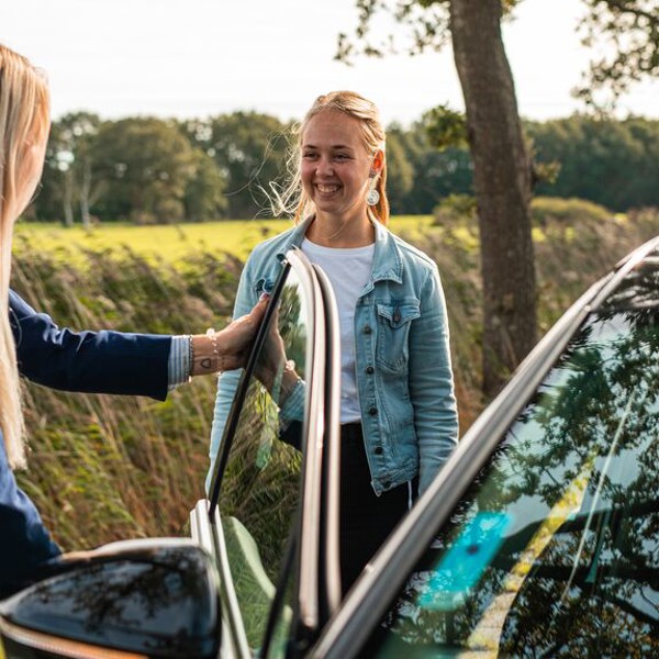 Twee jonge vrouwen staan lachen bij het open portier van een auto. Twee jonge vrouwen staan lachen bij het open portier van een auto.
