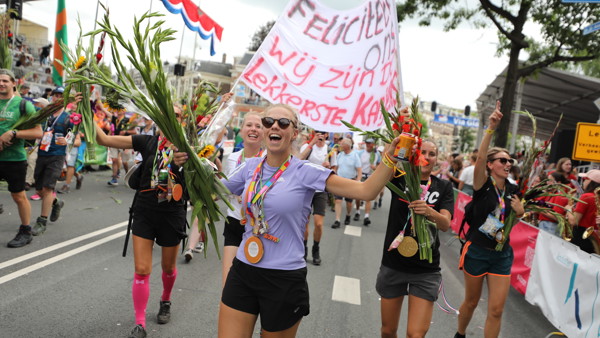 Juichende vrouwelijke deelnemers aan de Vierdaagse zijn net gefinished en dragen hun medaille en hebben gladiolen en een groot spanddoek vast. Juichende vrouwelijke deelnemers aan de Vierdaagse zijn net gefinished en dragen hun medaille en hebben gladiolen en een groot spanddoek vast.