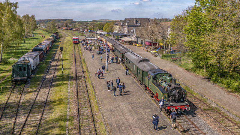 Een groen stoomtrein met zes wagons staat op station Simpelveld, er lopen allemaal mensen langs de trein. Een groen stoomtrein met zes wagons staat op station Simpelveld, er lopen allemaal mensen langs de trein.