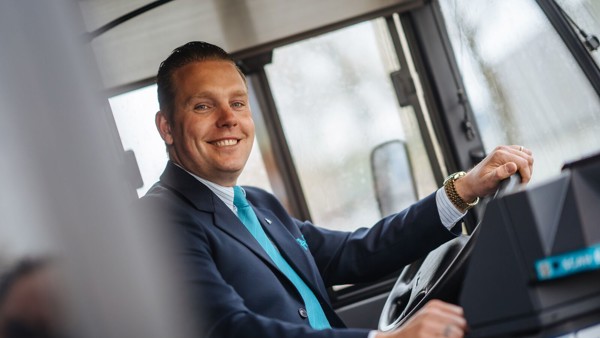 Buschauffeur in uniform zit achter het stuur van zijn Arriva-bus en kijkt lachend naar buiten. Buschauffeur in uniform zit achter het stuur van zijn Arriva-bus en kijkt lachend naar buiten.