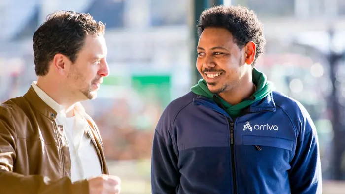 Een servicemedewerker van Arriva staat bij een halte en praat met een reiziger.