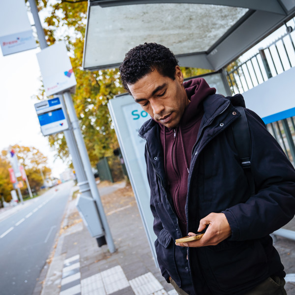 Een man staat bij een bushalte en kijkt op zijn telefoon. Een man staat bij een bushalte en kijkt op zijn telefoon.