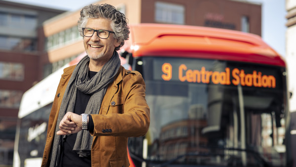 Man staat lachend op een station met een Arriva-bus met daarop '9 Centraal Station' achter hem. Man staat lachend op een station met een Arriva-bus met daarop '9 Centraal Station' achter hem.