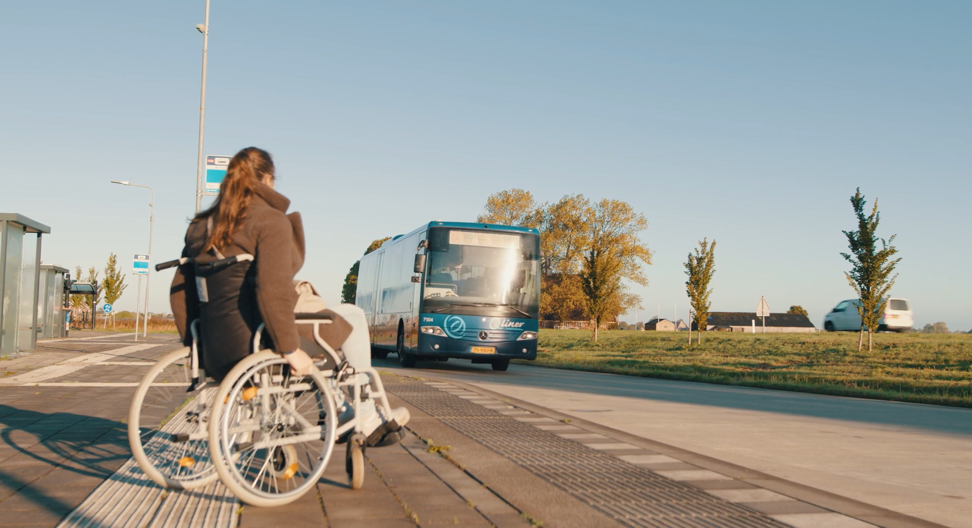 Reiziger in een rolstoel zit bij halte, bus komt aanrijden