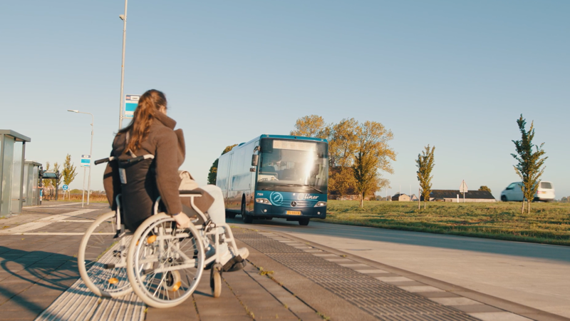 Reiziger in een rolstoel zit bij halte, bus komt aanrijden Reiziger in een rolstoel zit bij halte, bus komt aanrijden